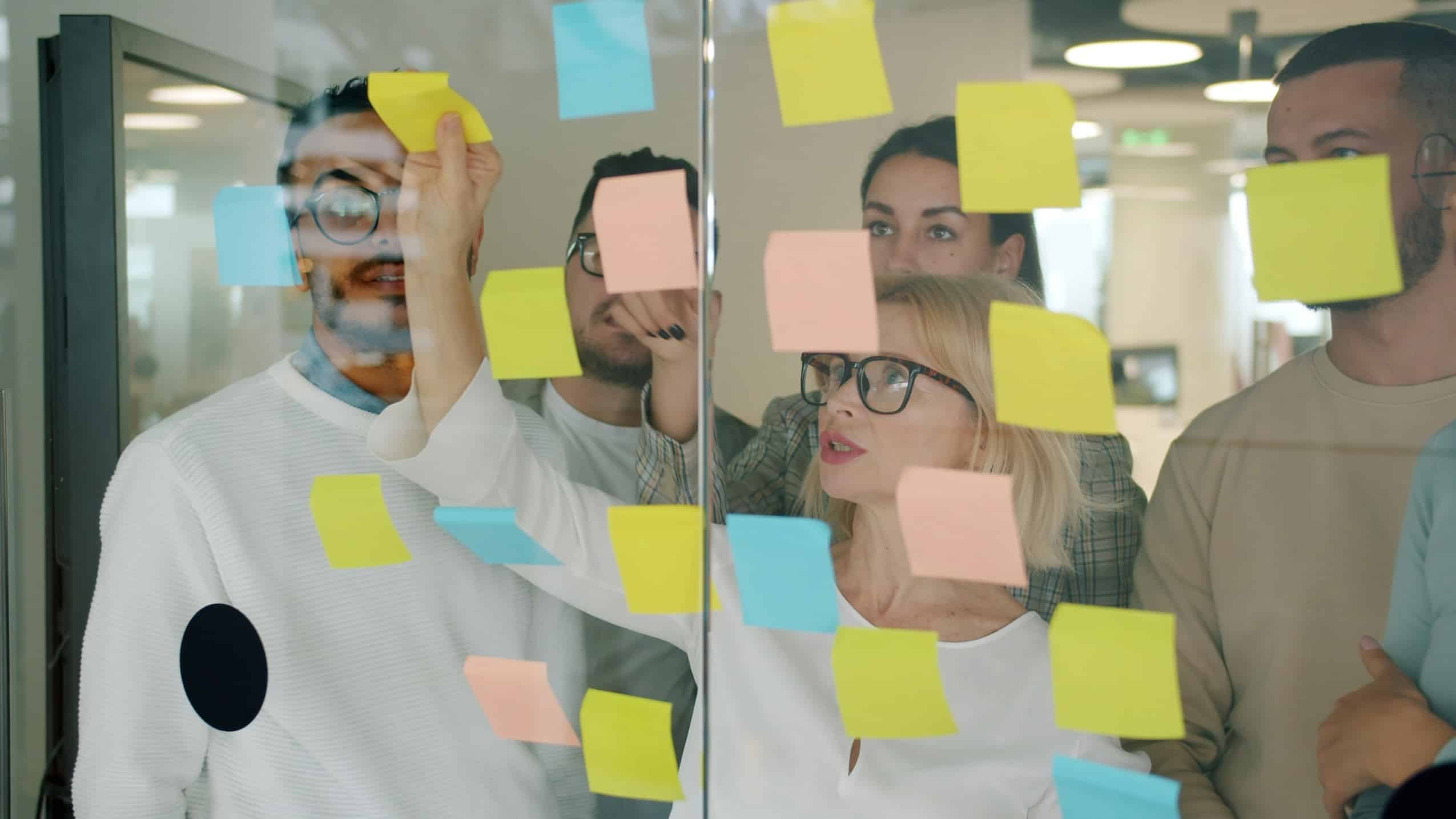 Team collaborating around a glass wall covered with colourful sticky notes during an agile workshop.