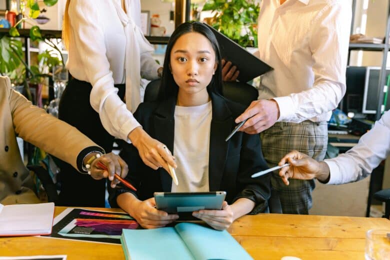 Young professional woman sitting calmly under pressure while colleagues ask for attention — symbolising leadership, multitasking, and resilience.